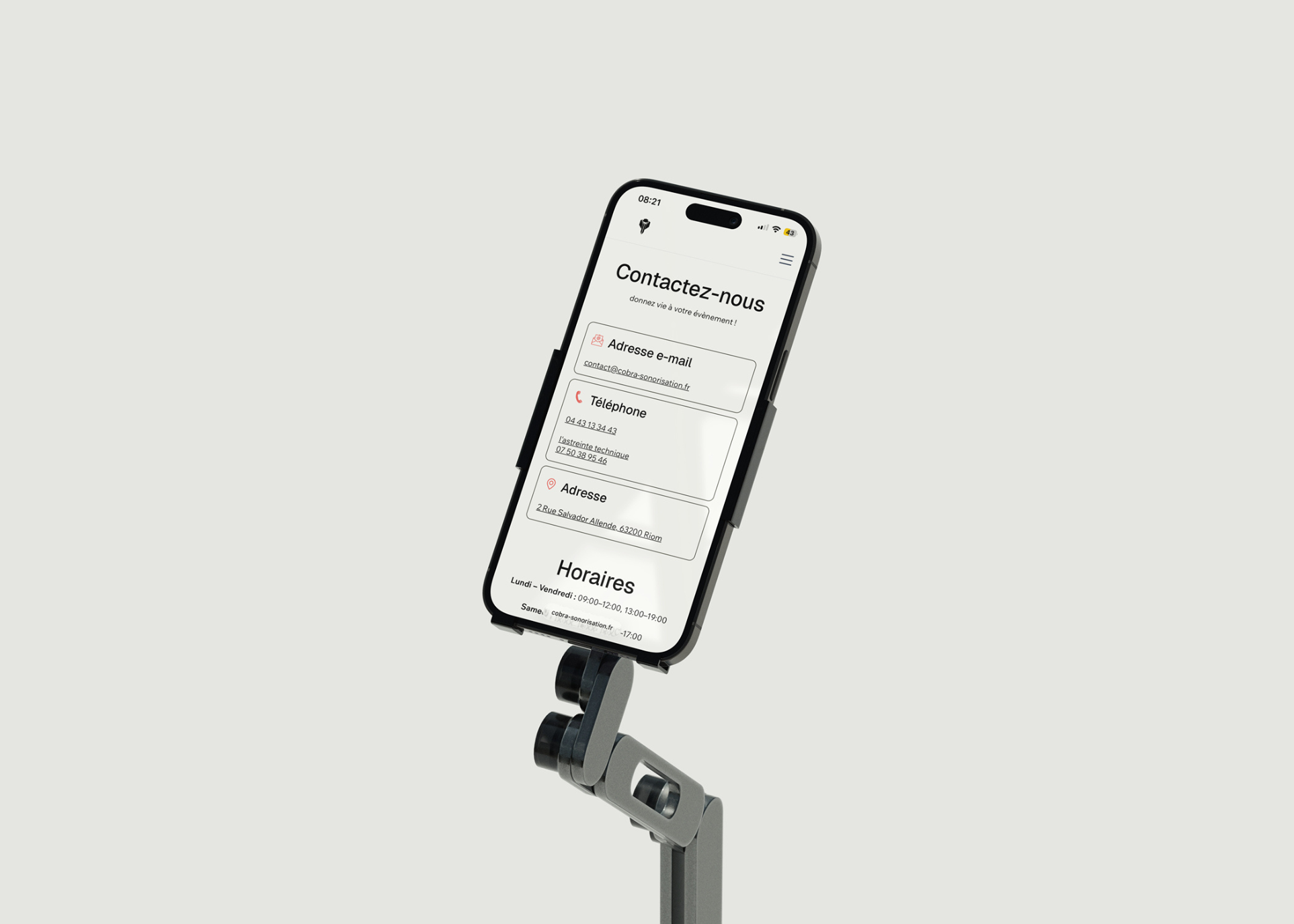 Téléphone noir sur support affichant une page de contact en français avec email, téléphone, adresse et horaires.