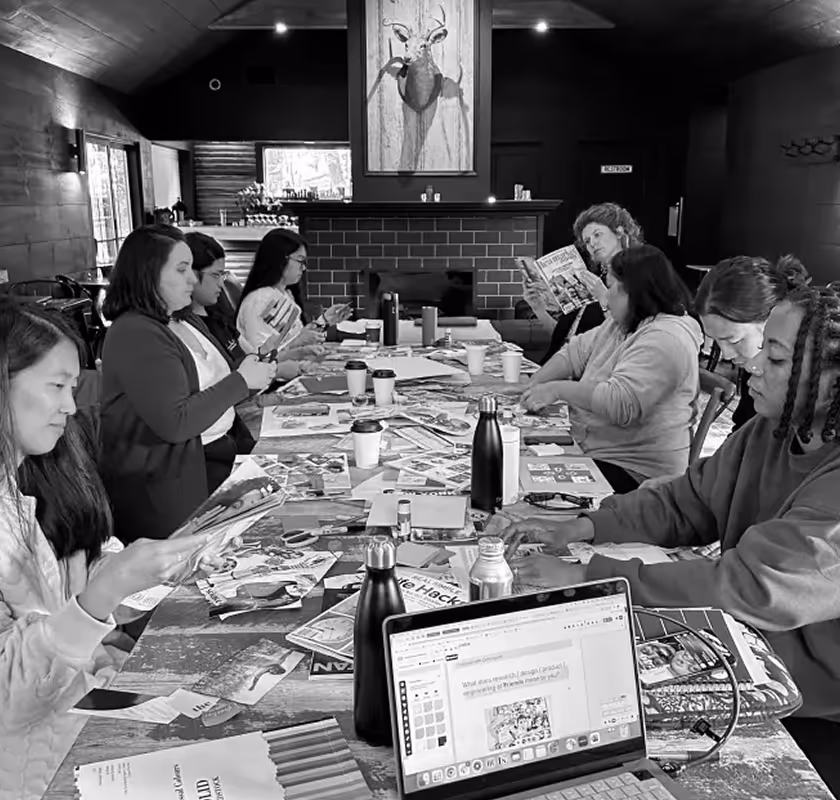 Group of people sitting around a table engaged in reading magazines and working on a laptop in a cozy room.