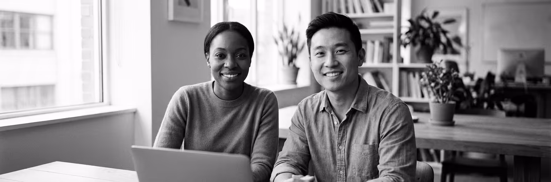 Smiling man and woman sitting together at a table with a laptop in a modern office.