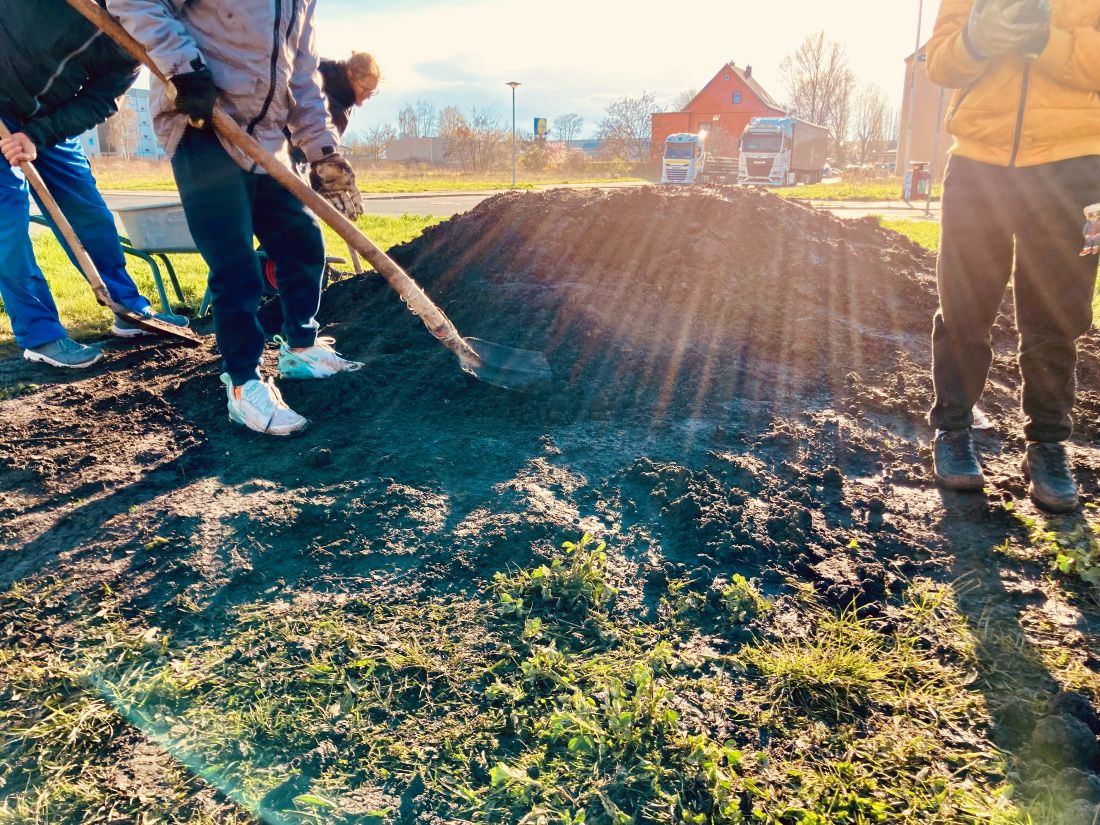 Menschen mit Schaufeln graben eine Grünfläche um