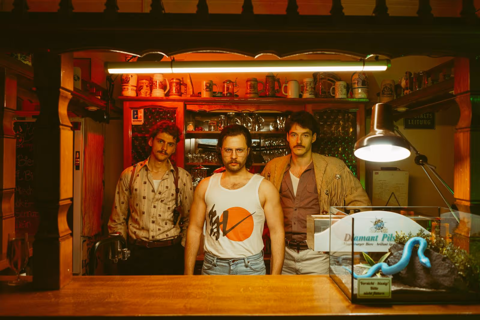 Federhall Foto. 3 Männer stehen unter Neonlichtröhre und schauen in die Kamera
