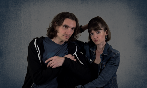 Nico Rivers und Emily Graham-Handley sitzen nebeneinander vor einem blau-grauen Hintergrund.