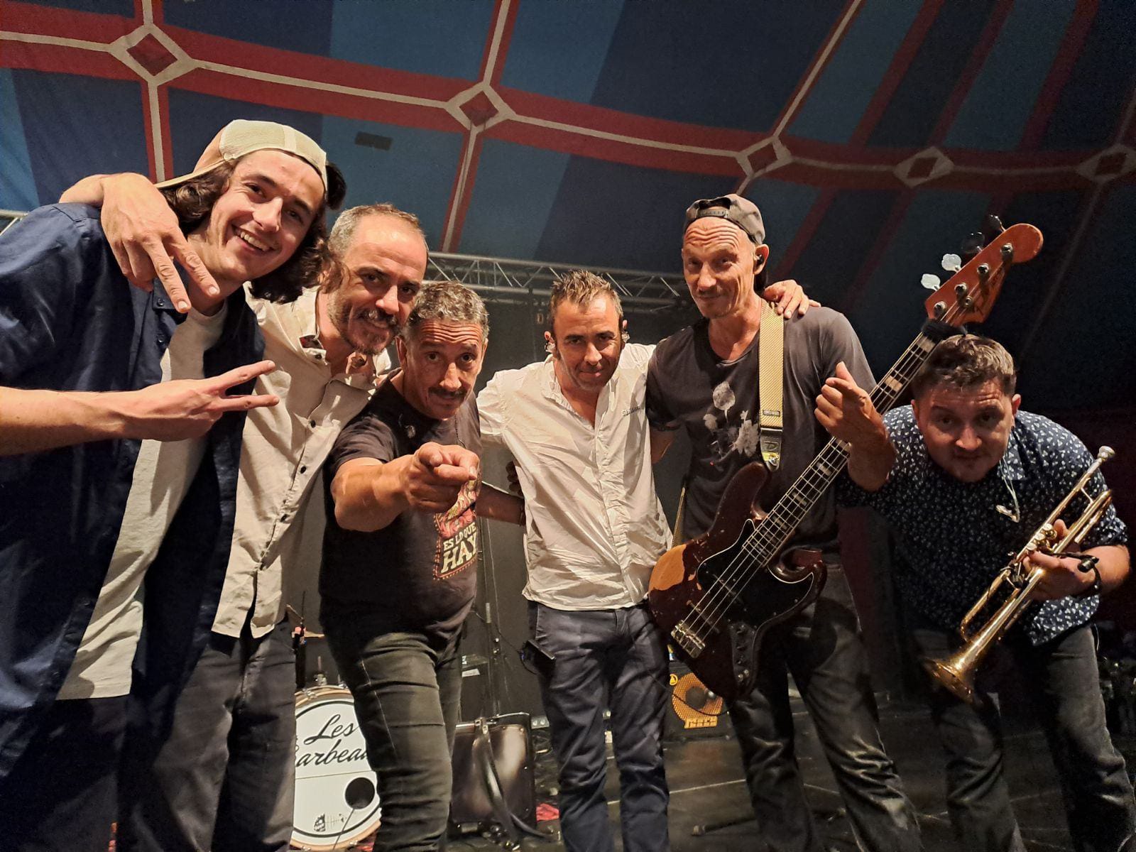 6 Musiker mit Instrumenten halten sich im Arm und schauen direkt in die Kamera.