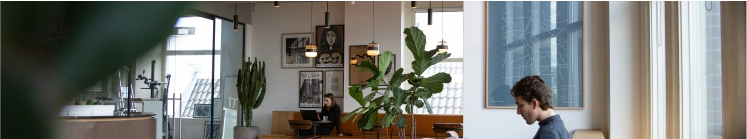 Modern café interior with green plants, large windows, and people working on laptops.