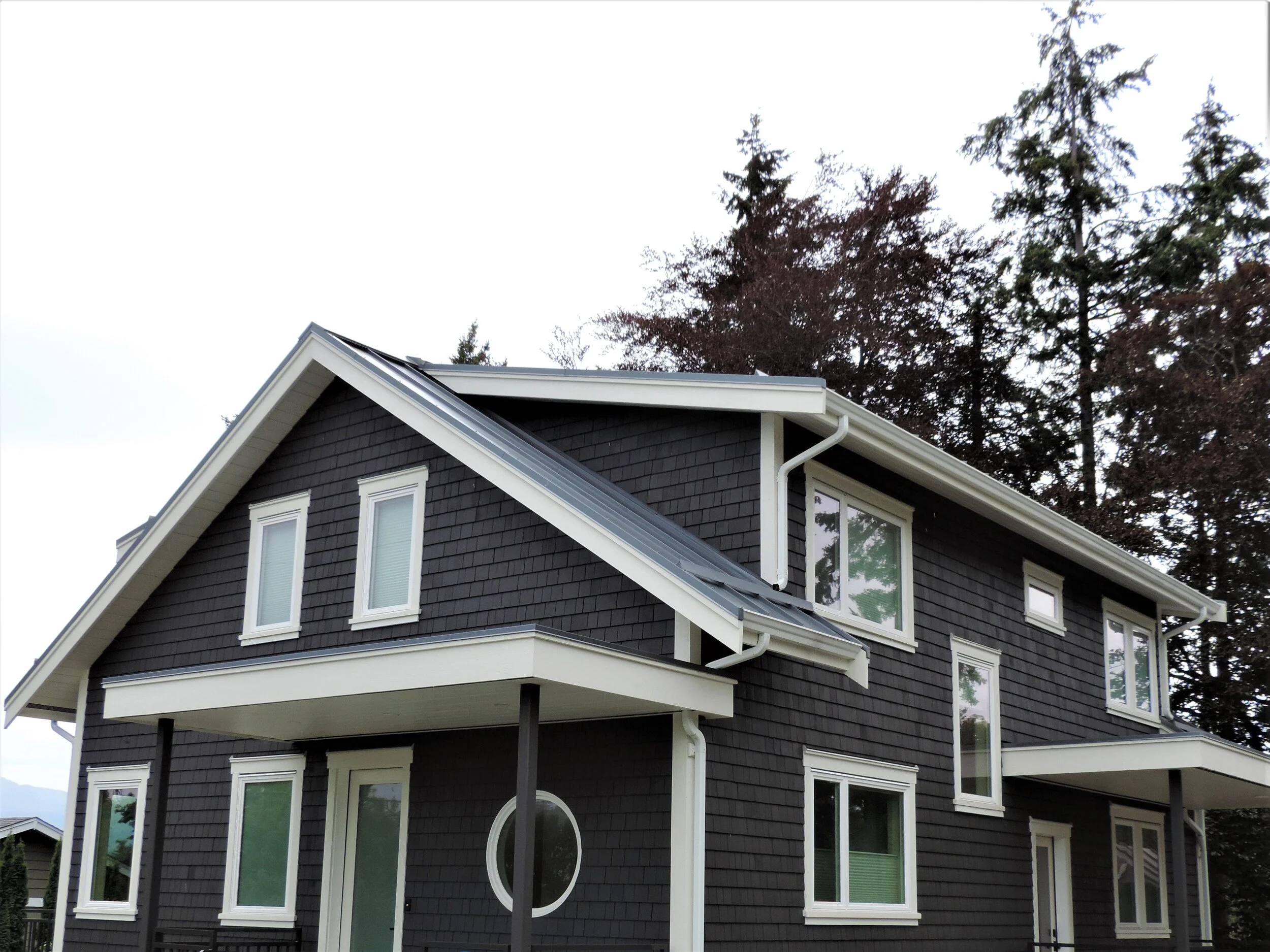 Residential roof on Vancouver Island showing heavy moss growth along shaded shingle runs and debris accumulation in the gutters