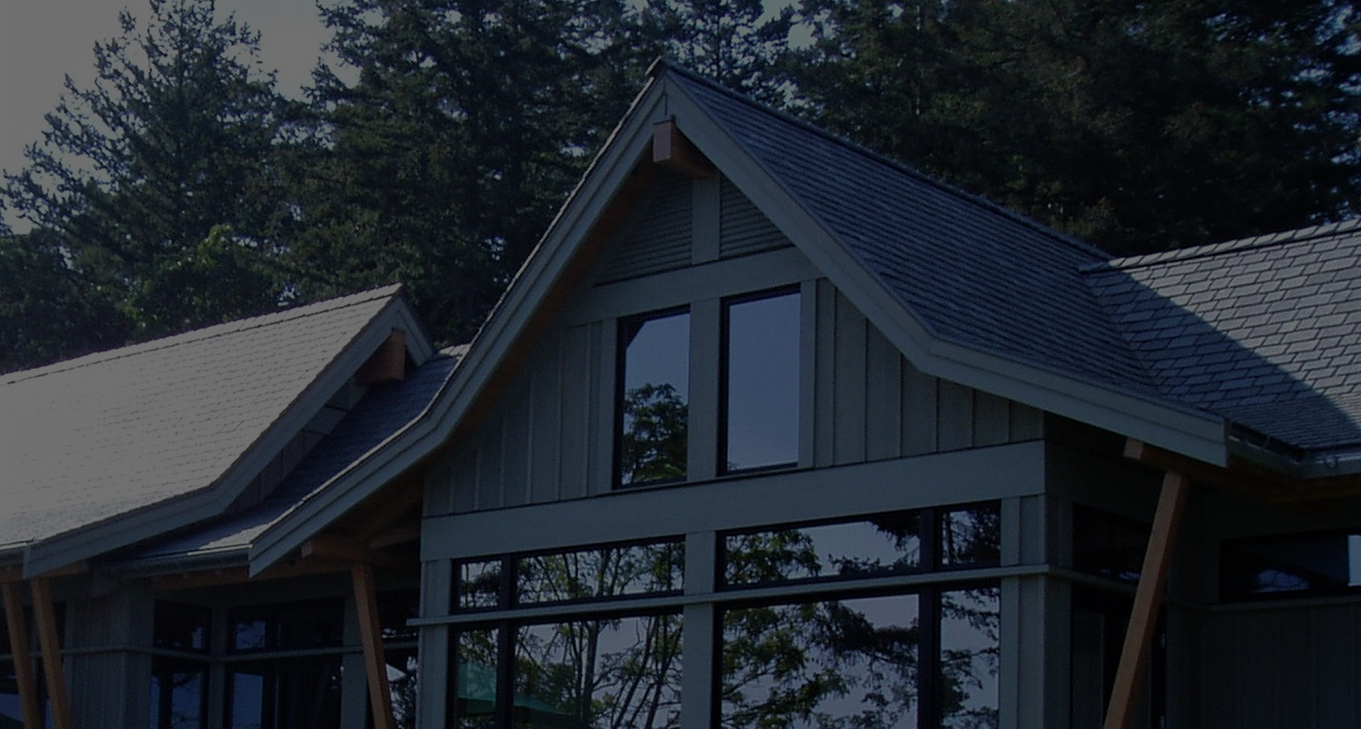 steep gable roof with dark asphalt shingles over vertical wood siding at dusk