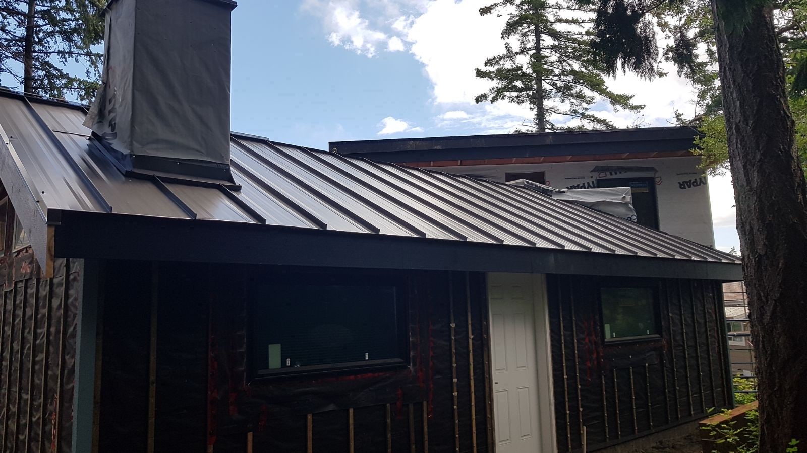 dark standing seam metal roof on a house under construction with black weather-resistive wrap on the walls