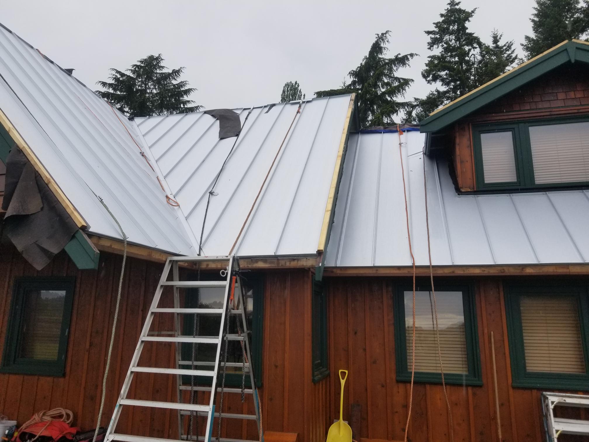 standing seam metal roof panels on a steep pitched roof with ladder access and safety ropes
