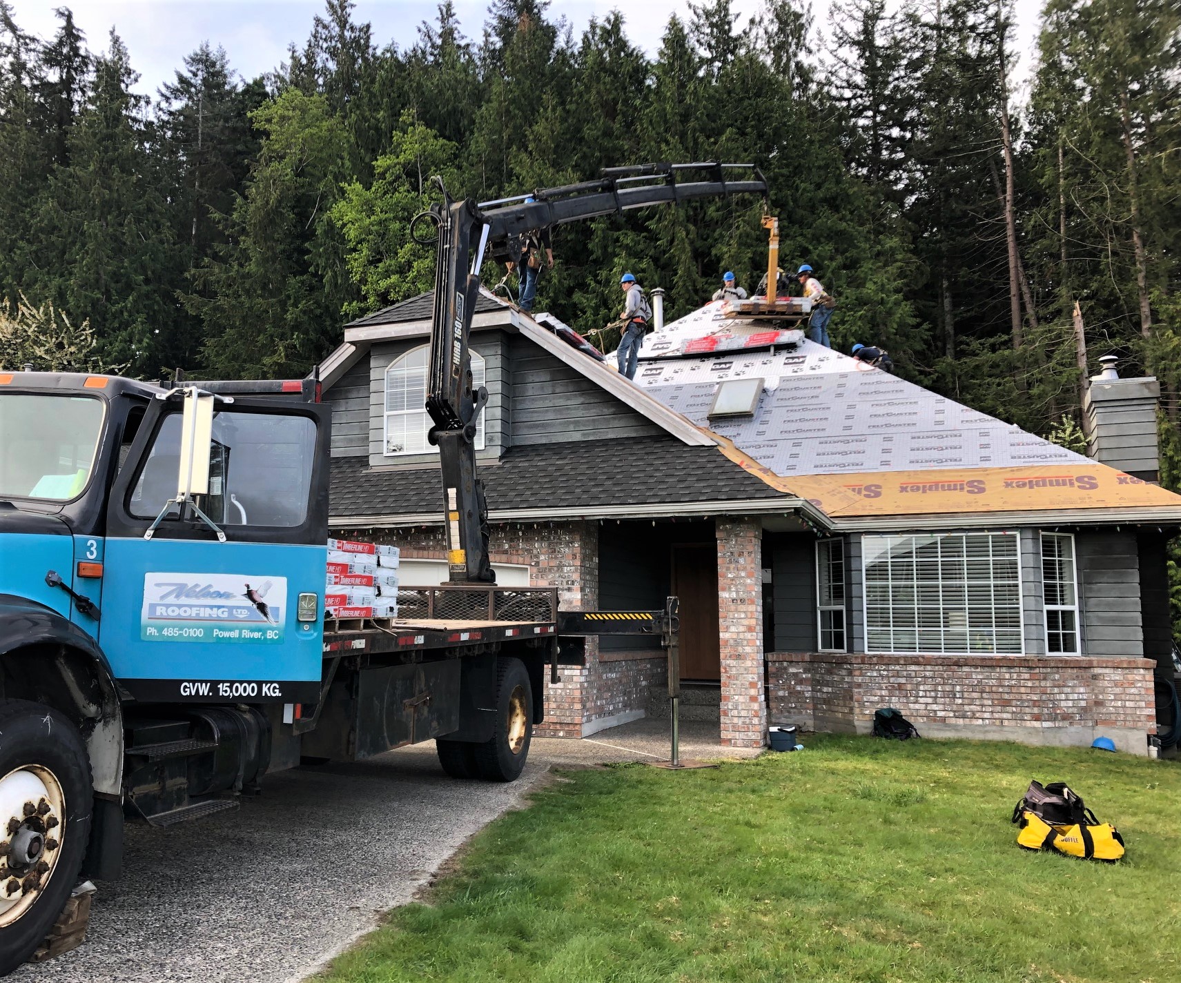 boom truck crane lifting shingle bundles to a crew installing a new asphalt shingle roof