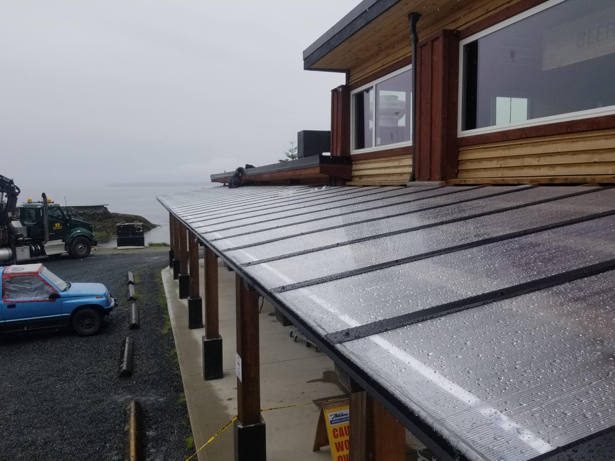 ribbed metal roof panels on a waterfront building, rain visible, a boom truck parked below