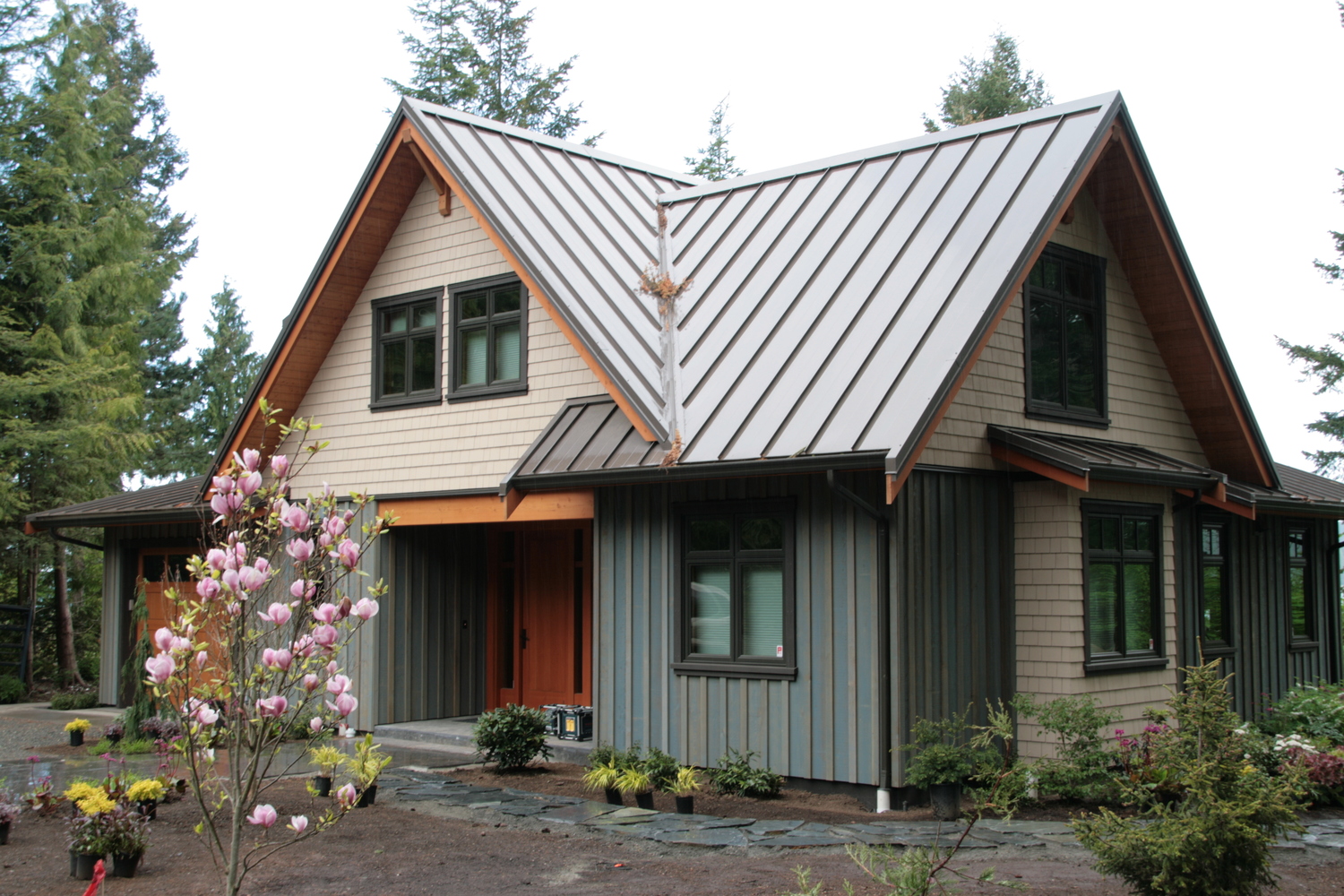 gray standing seam metal roof over a two-story home with wood siding and a blooming magnolia tree in front