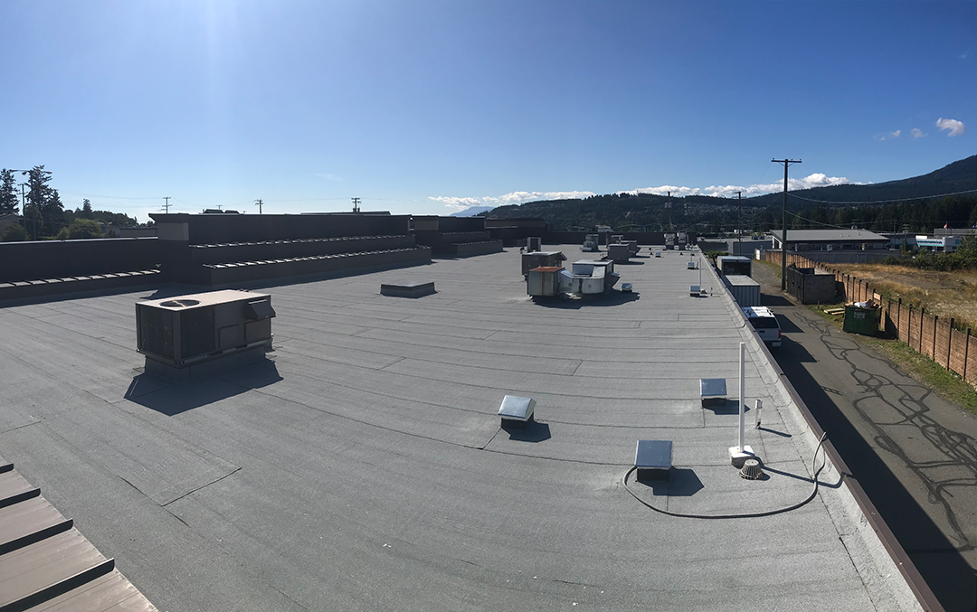 flat membrane roof with rooftop HVAC units and vent stacks, mountains in the distance