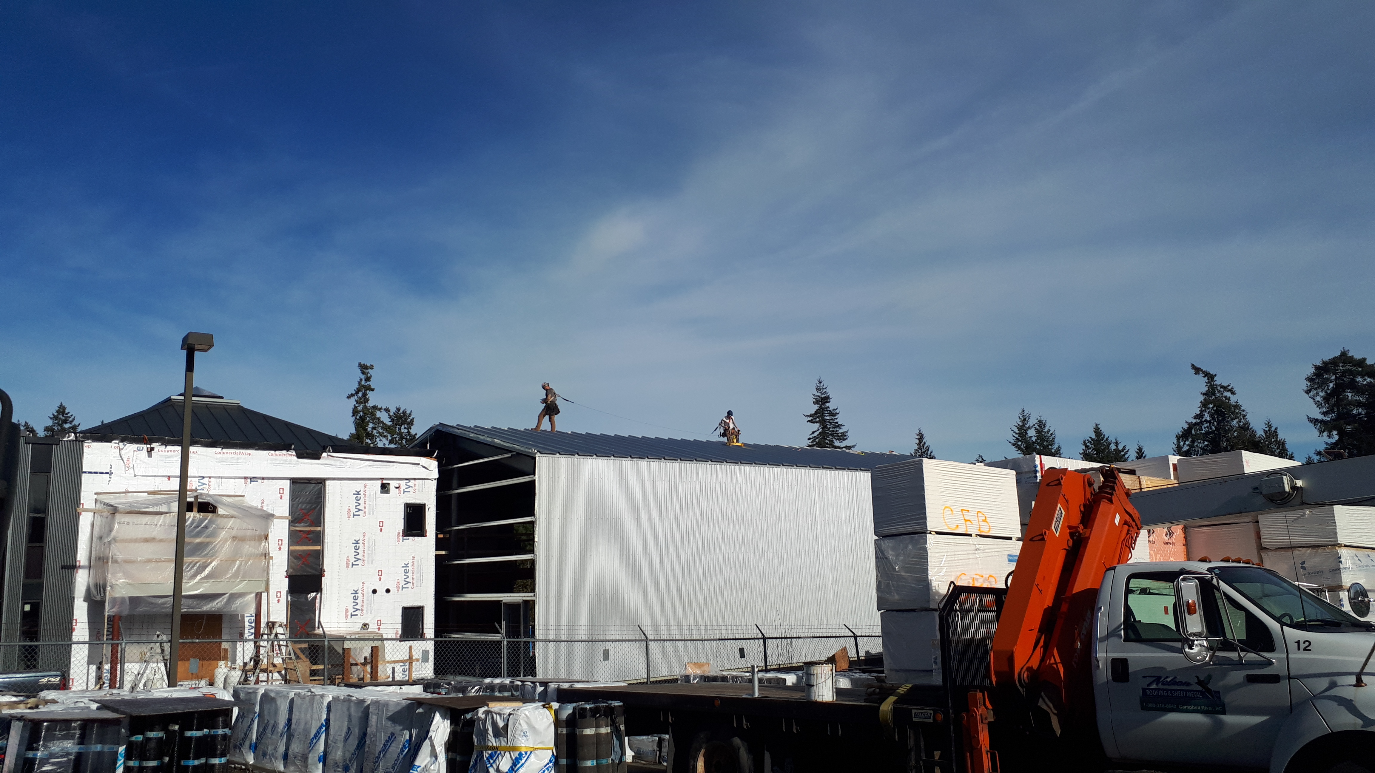 workers on safety lines walking a metal roof above a building clad in flat metal panels
