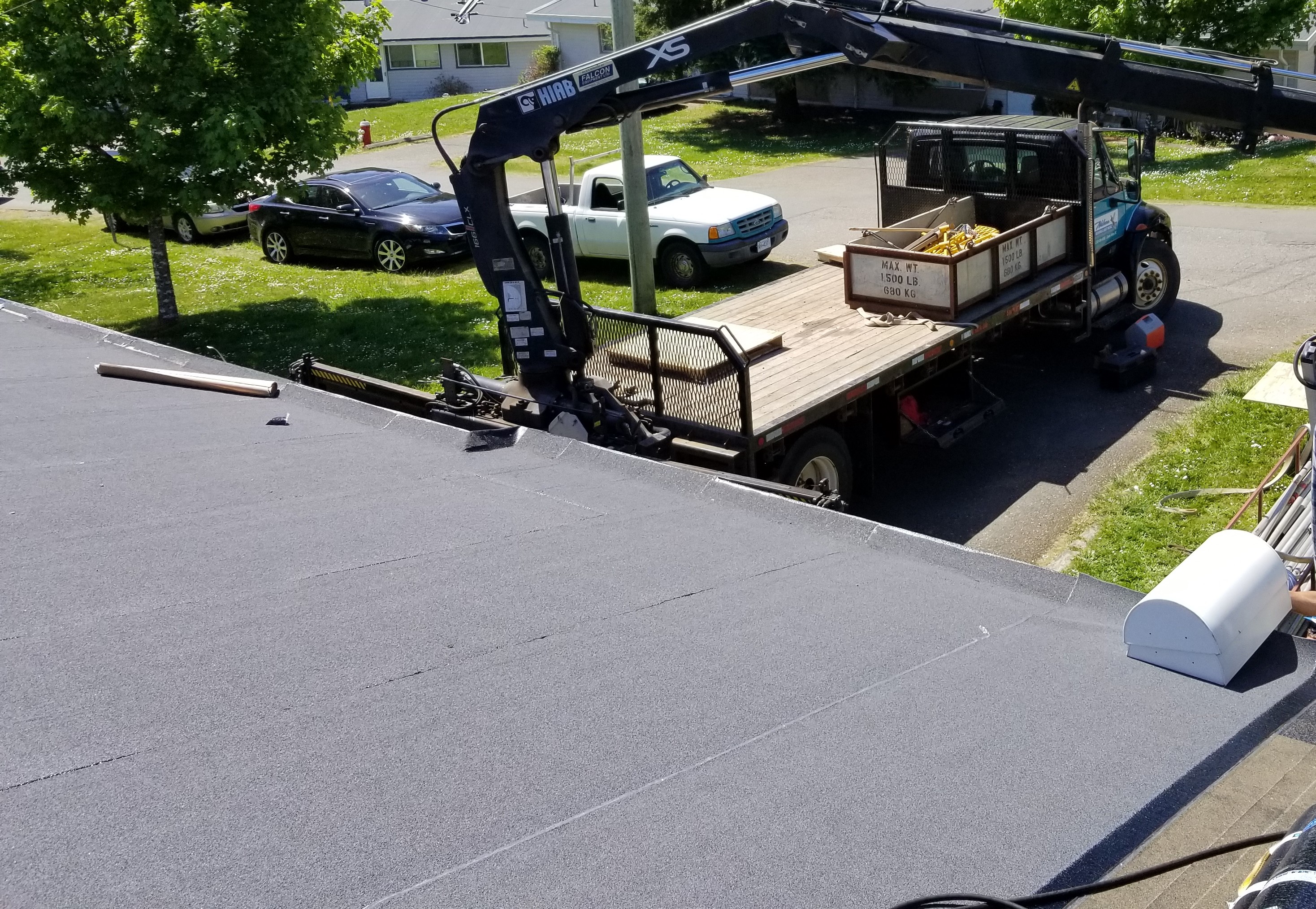 black roofing membrane on a flat roof with a crane truck parked in the driveway below