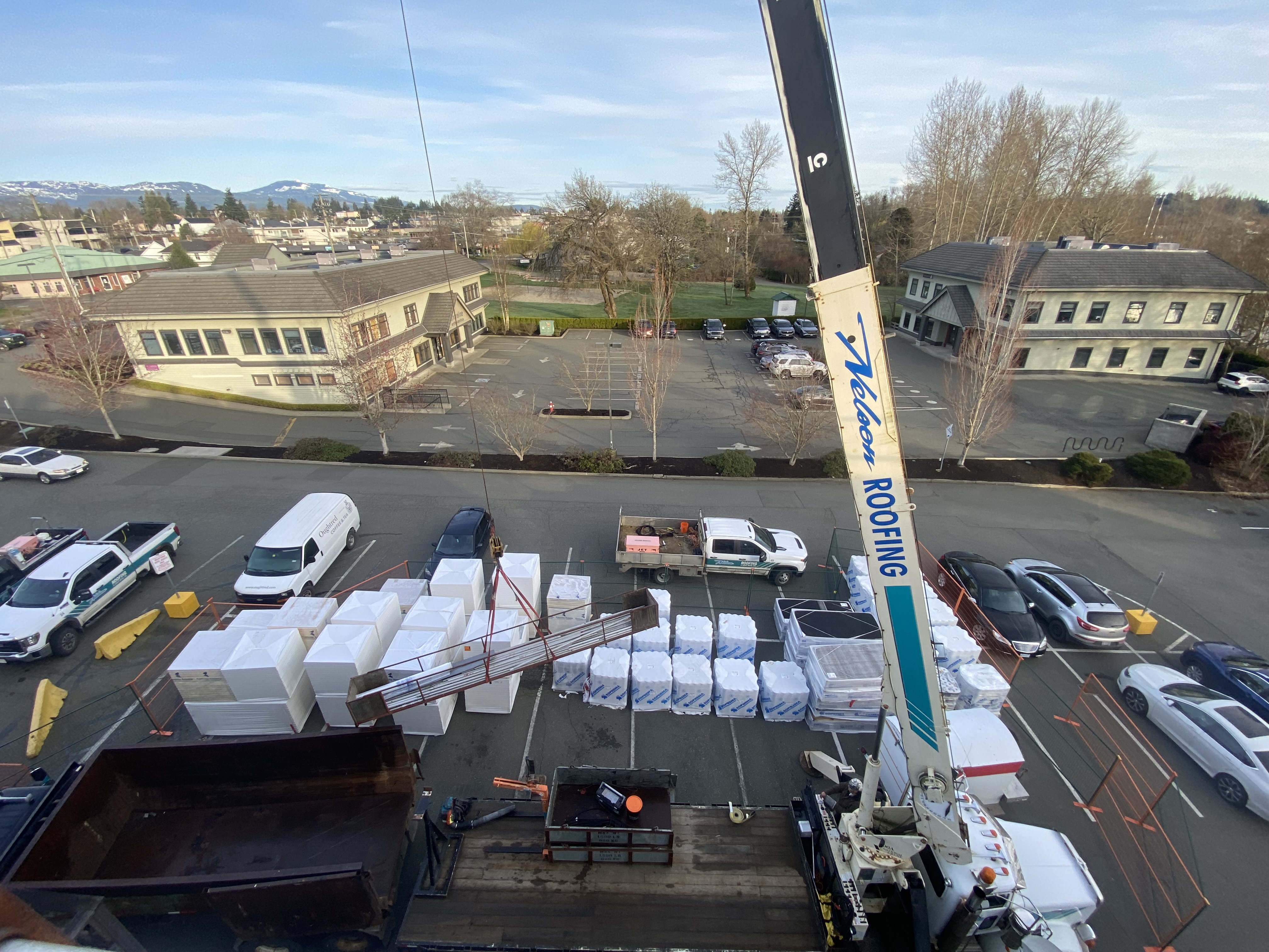 boom truck lifting roofing material bundles staged in a parking lot