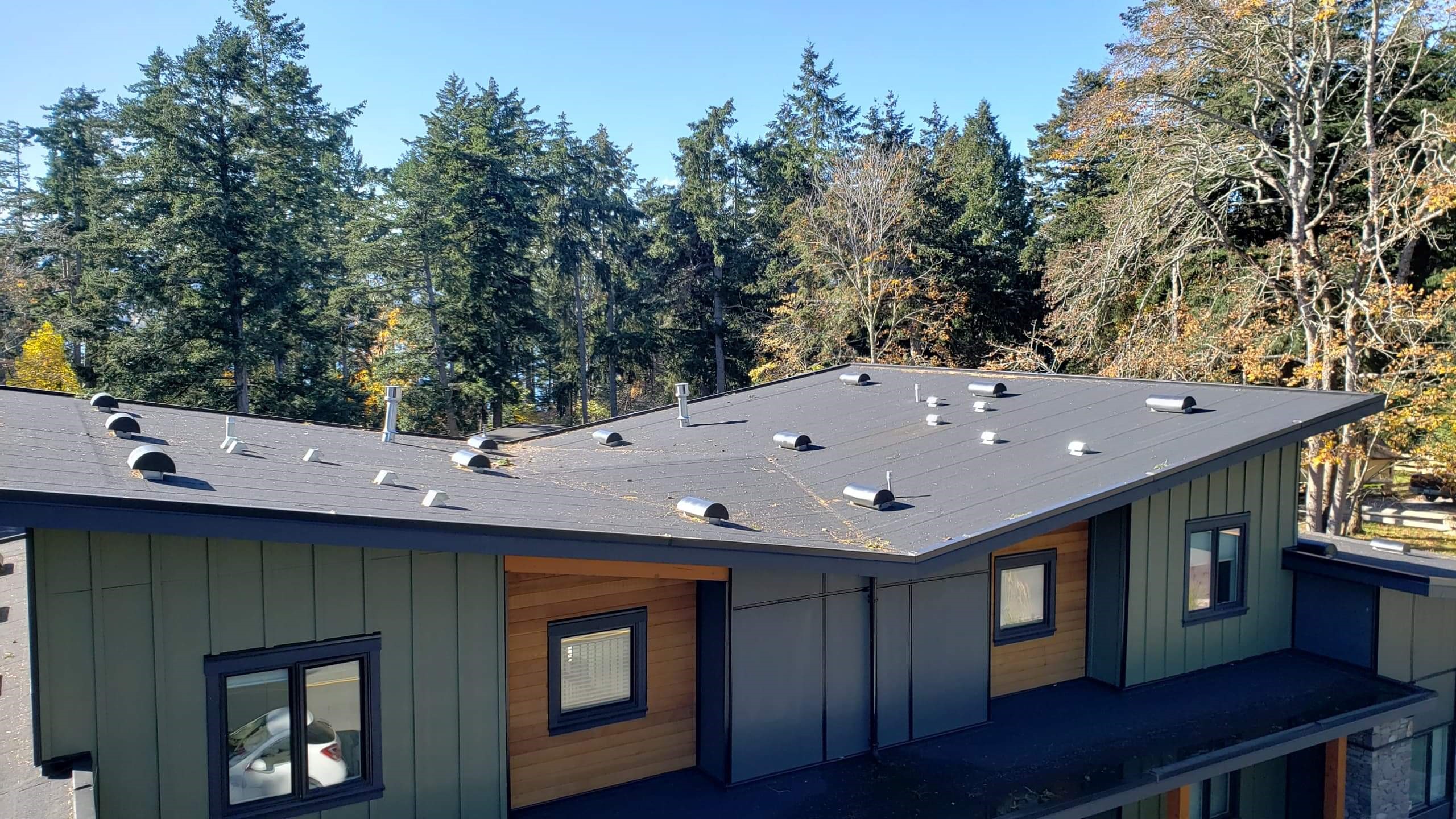 standing seam metal roof in dark charcoal on a home with green board and batten siding