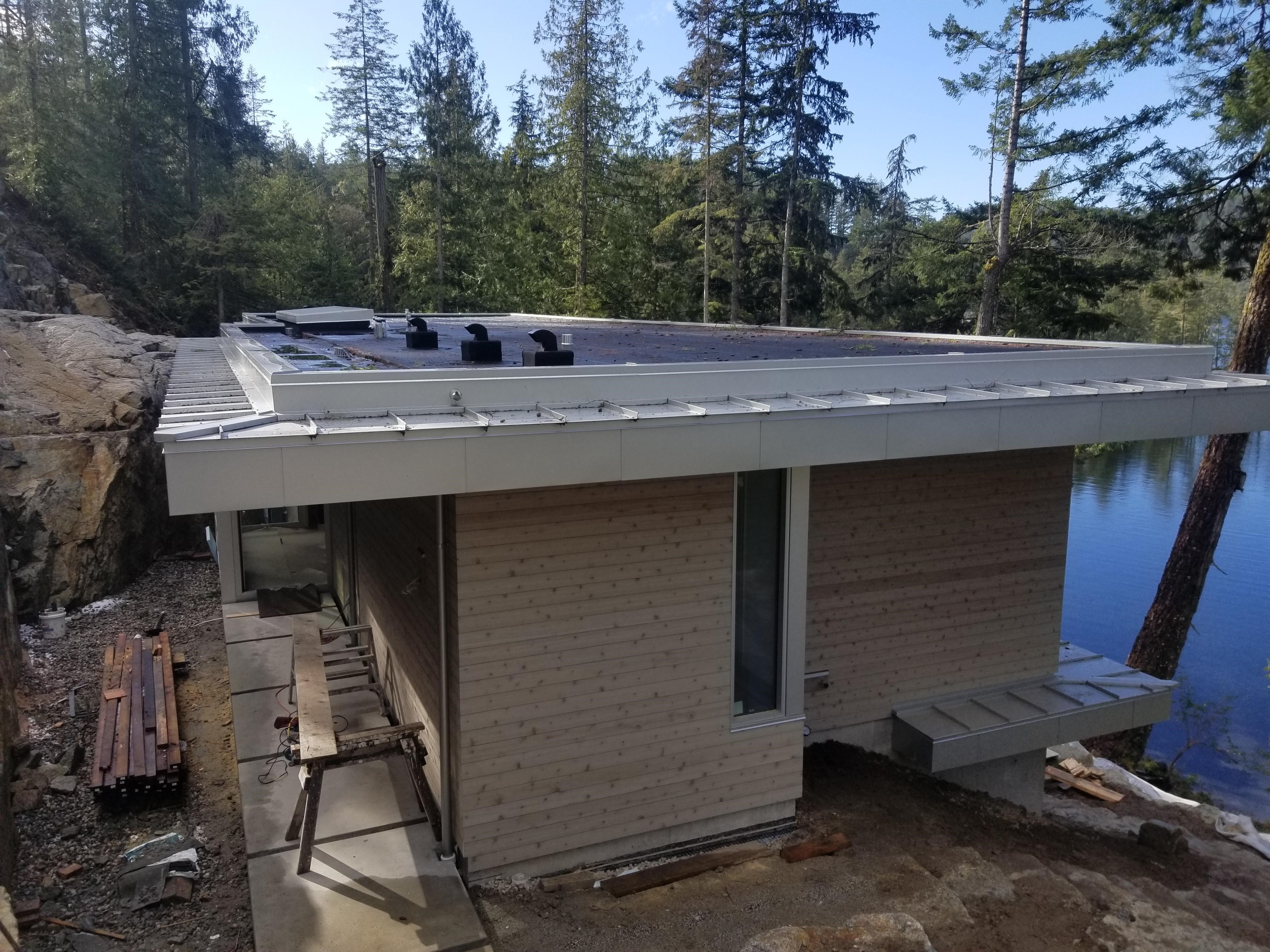 flat roof membrane on a lakeside home under construction with rock cliff nearby