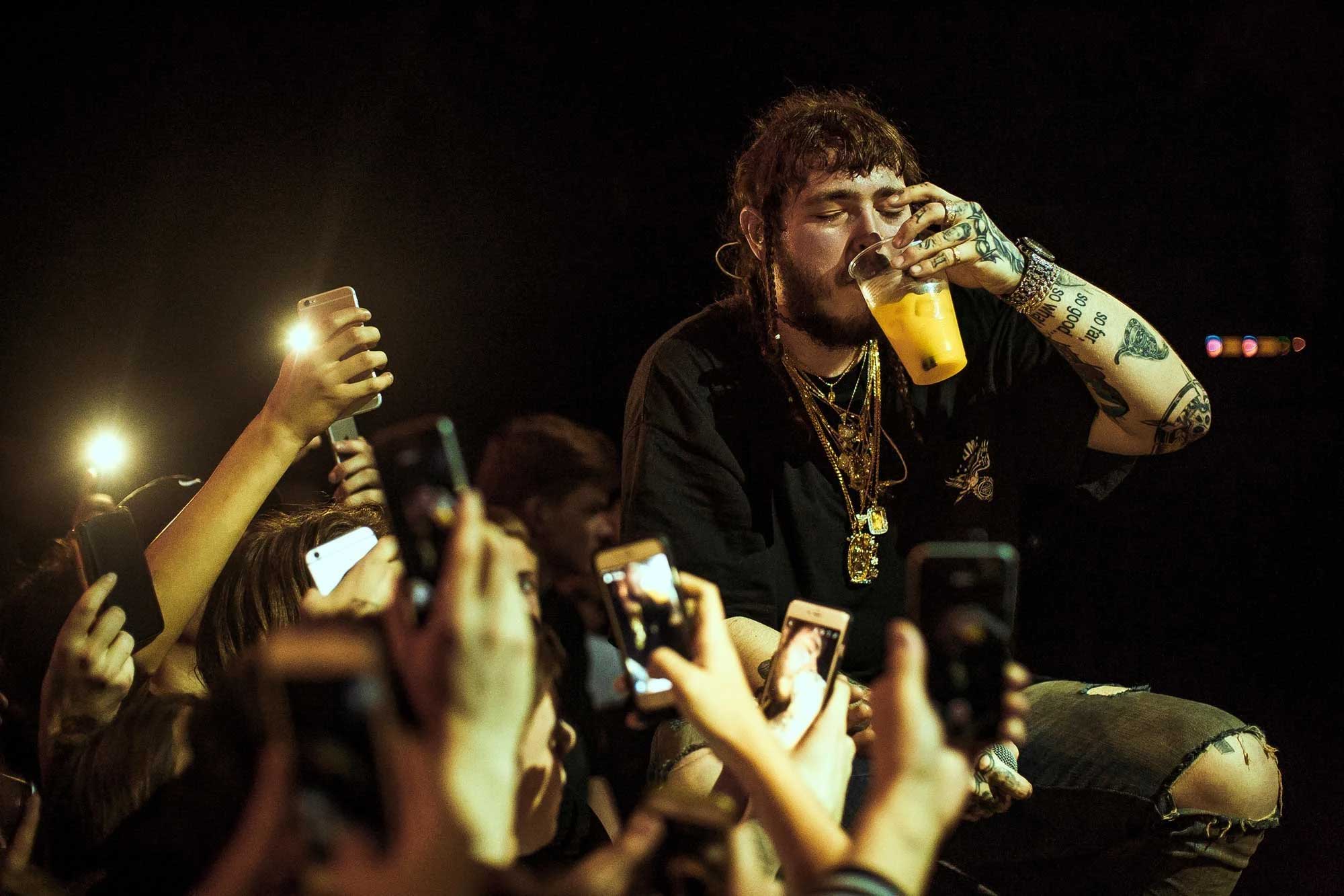 Post Malone takes a sip of a drink while on stage with front-row fans