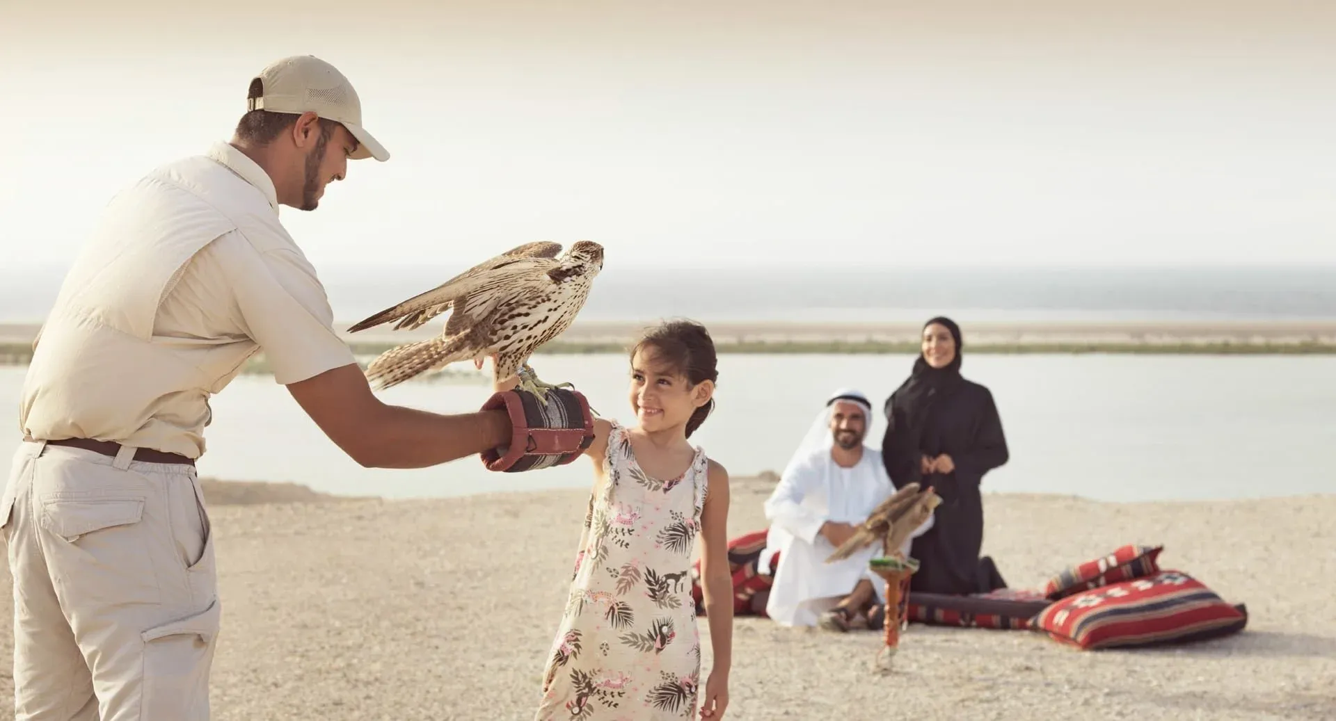 A falcon handler helps a young girl hold the bird