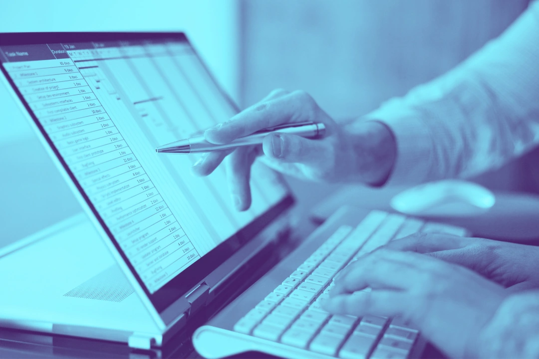 close-up photo of a computer on which one person is typing and another person is pointing at something on the screen