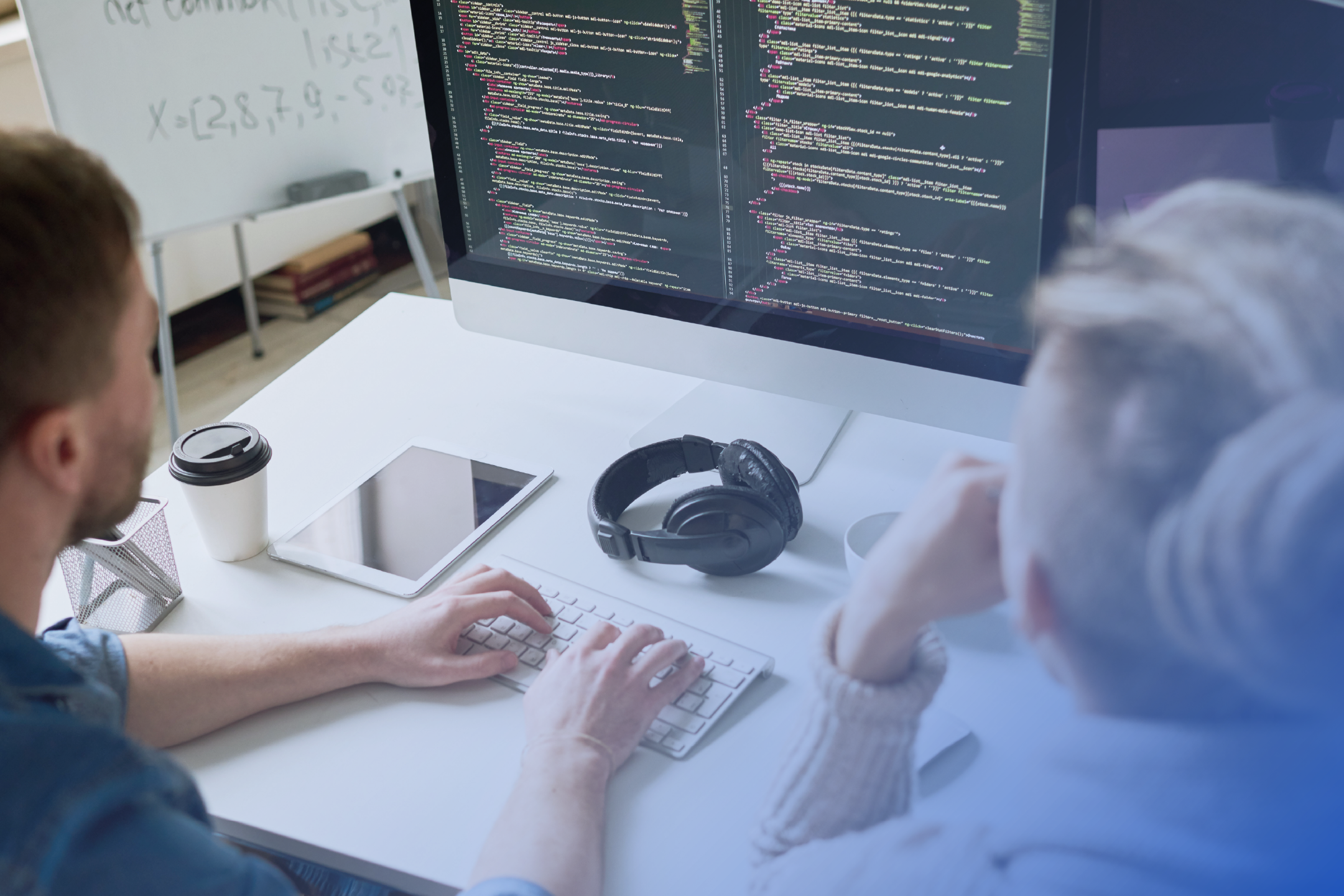 Two professionals sitting at a desk, reviewing software code displayed on a computer screen 