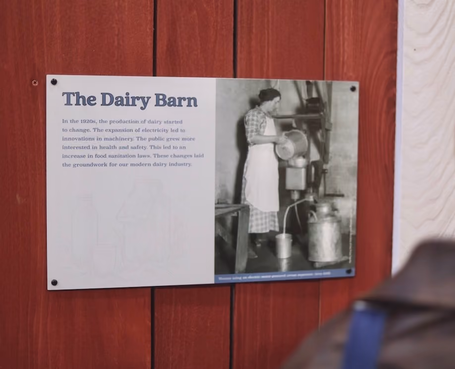 Informational sign titled 'The Dairy Barn' with text and an old photo of a woman pouring milk in a dairy setting.