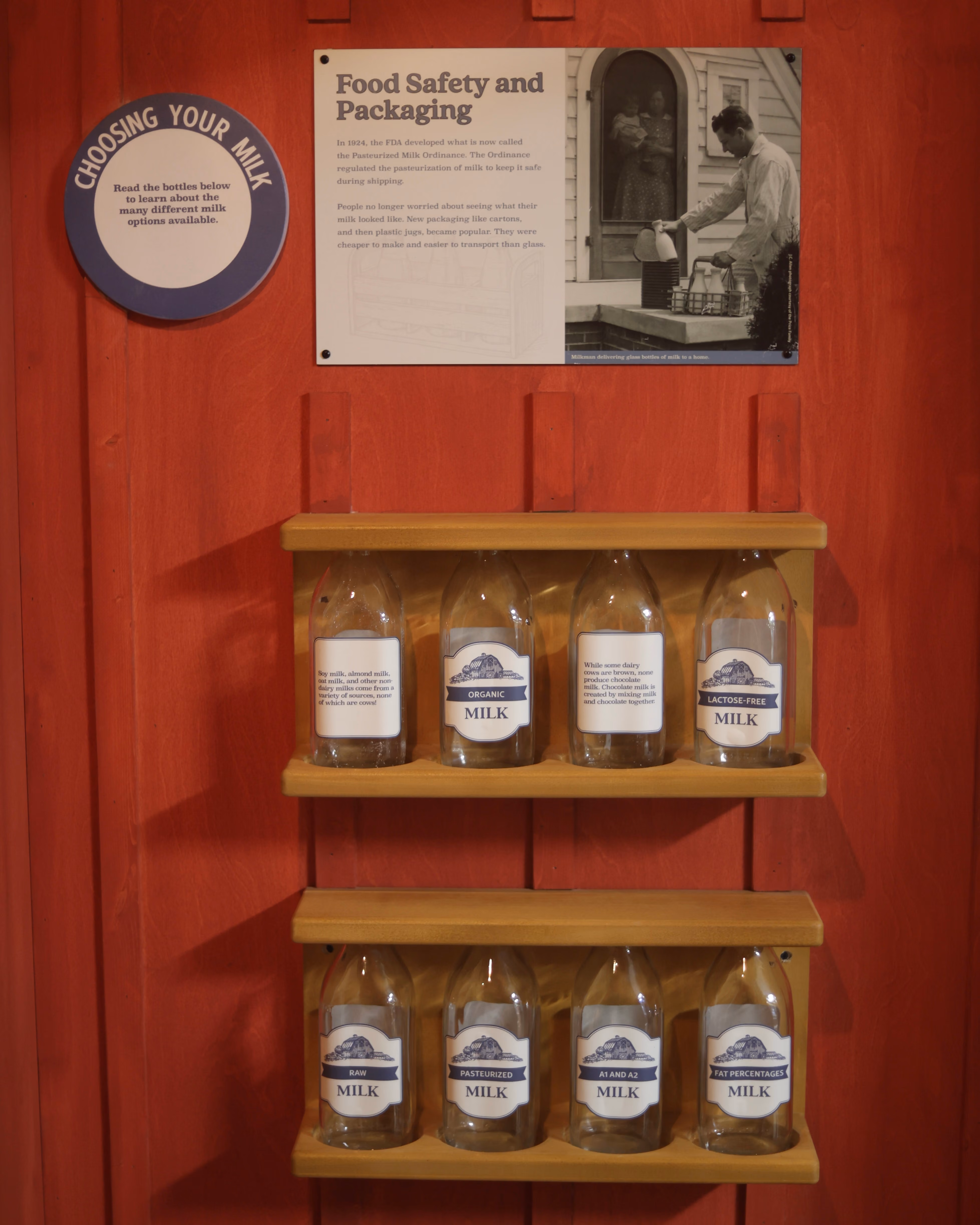 Display of eight labeled milk bottles on wooden shelves with a sign titled Food Safety and Packaging.