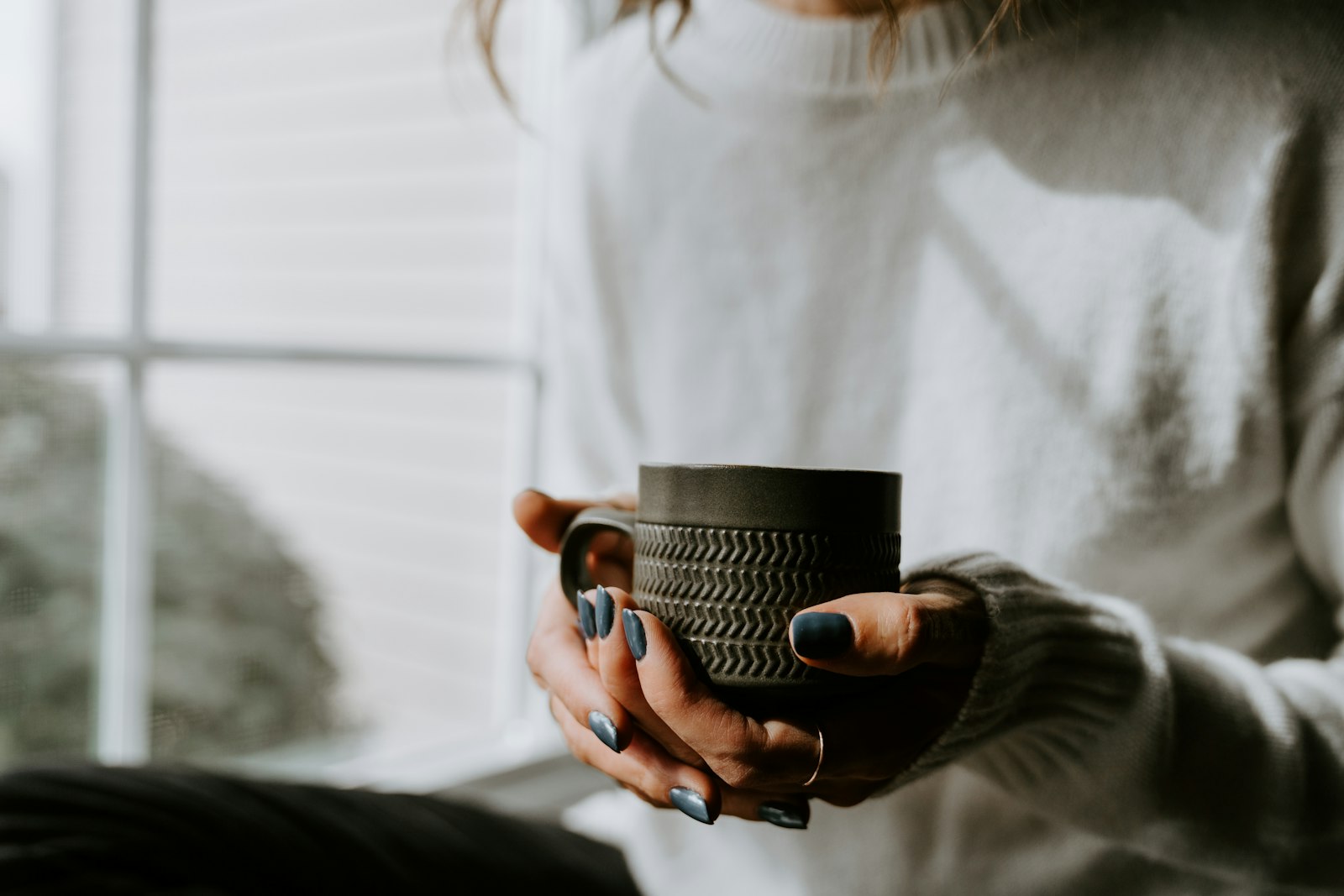 Woman holding a coffee cup in her hands at home illustrating lifestyle causes of yellow teeth