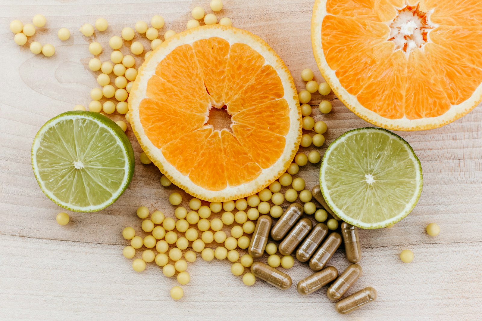 Citrus slices, small yellow supplement beads and brown capsules on wood, showing vitamin formats that may affect teeth