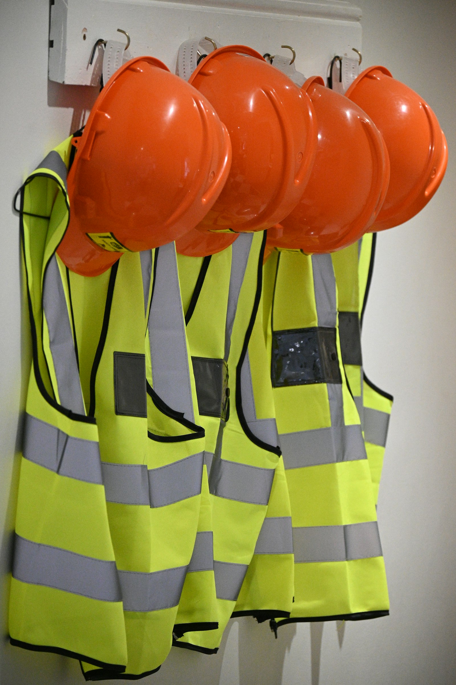 Hard hats and hi-vis vests hanging on a wall on a construction site, a reminder of tradie dental health and workplace safety