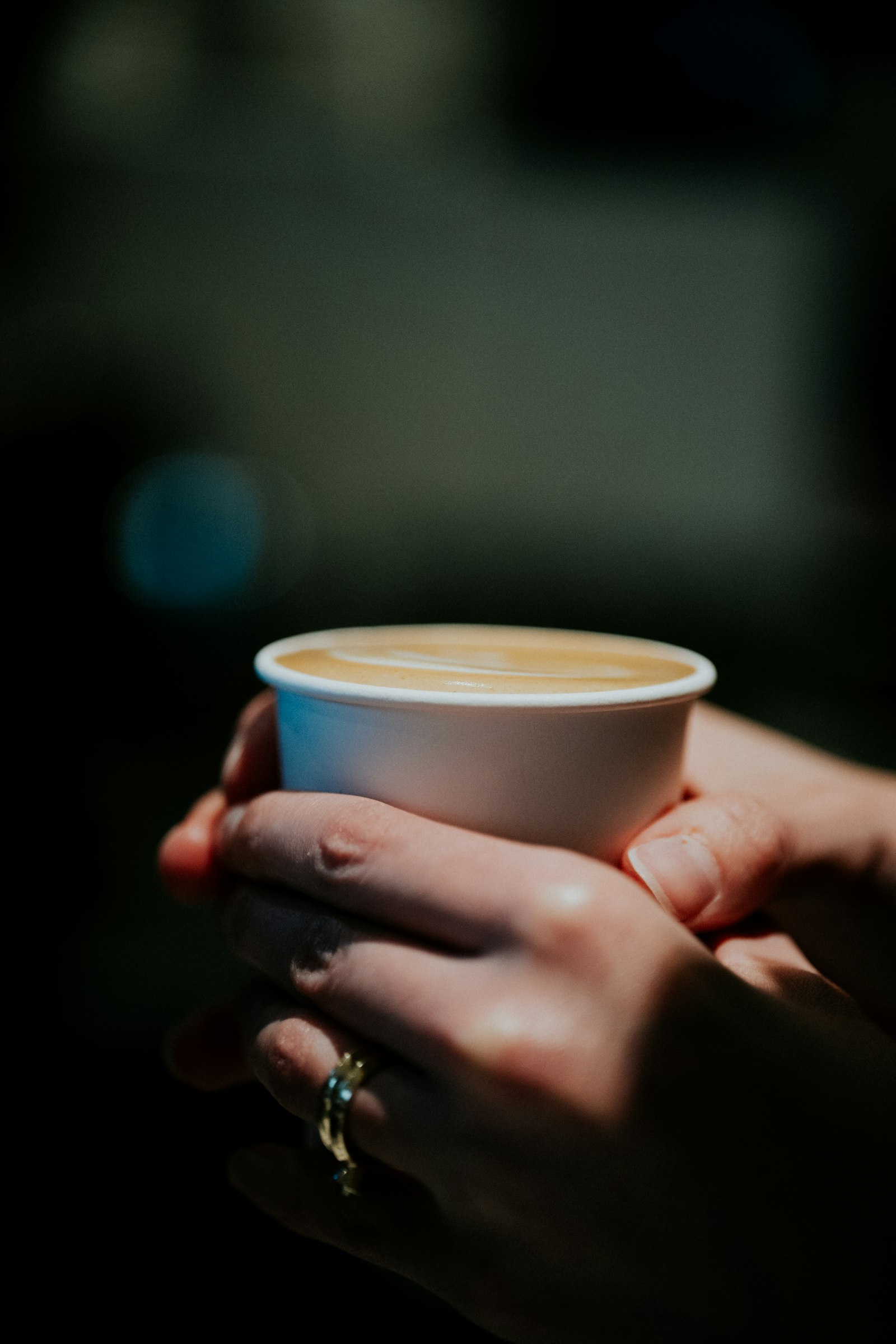 Hands holding a takeaway latte, a common part of a working day that shapes dental health at work by occupation