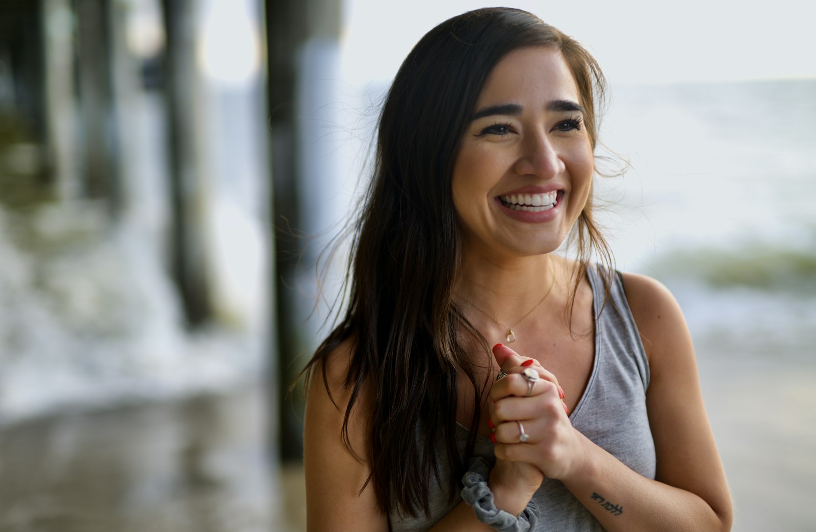 Woman with long dark hair smiling broadly outdoors near the water