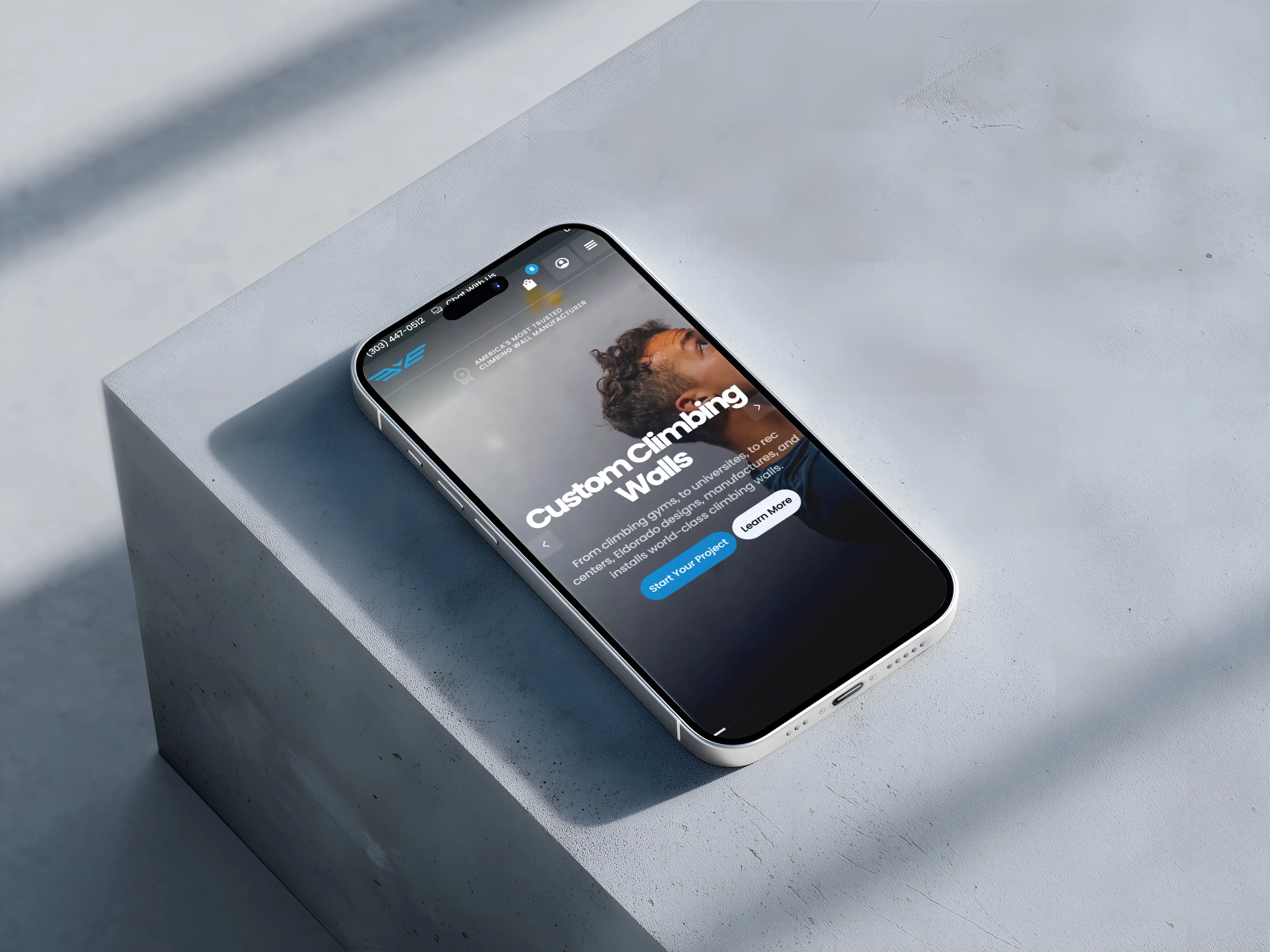 Smartphone displaying a website page about custom climbing walls with a man looking up in the background.