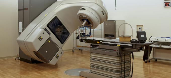 Medical linear accelerator machine in a radiation therapy room with a treatment table.