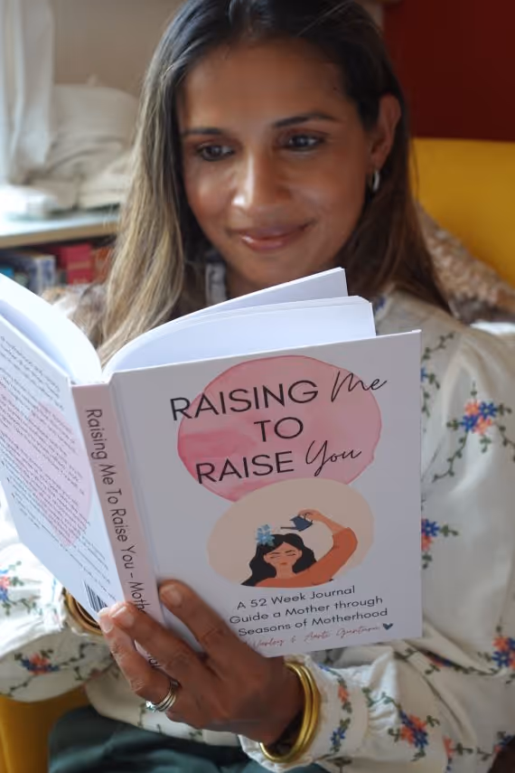 Woman reading a book titled 'Raising Me to Raise You: A 52 Week Journal Guide a Mother through Seasons of Motherhood.'