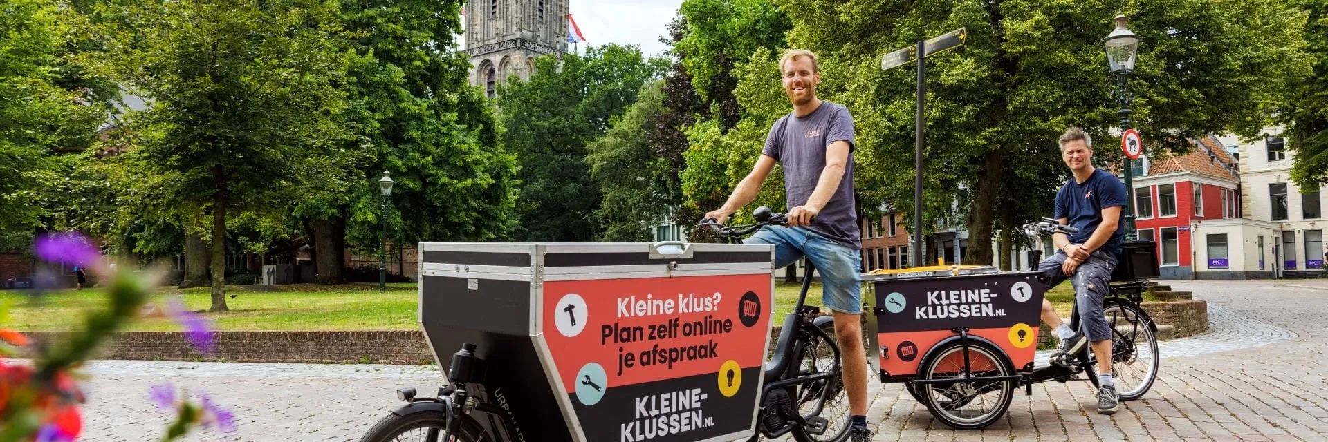 Een wijds uitzicht op een straatbeeld met bomen en een gebouw op de achtergrond. Een man staat in de buurt van een fiets.