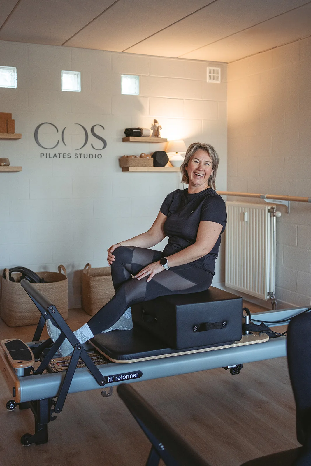 Une dame souriante sur une machine de Pilates Reformer.