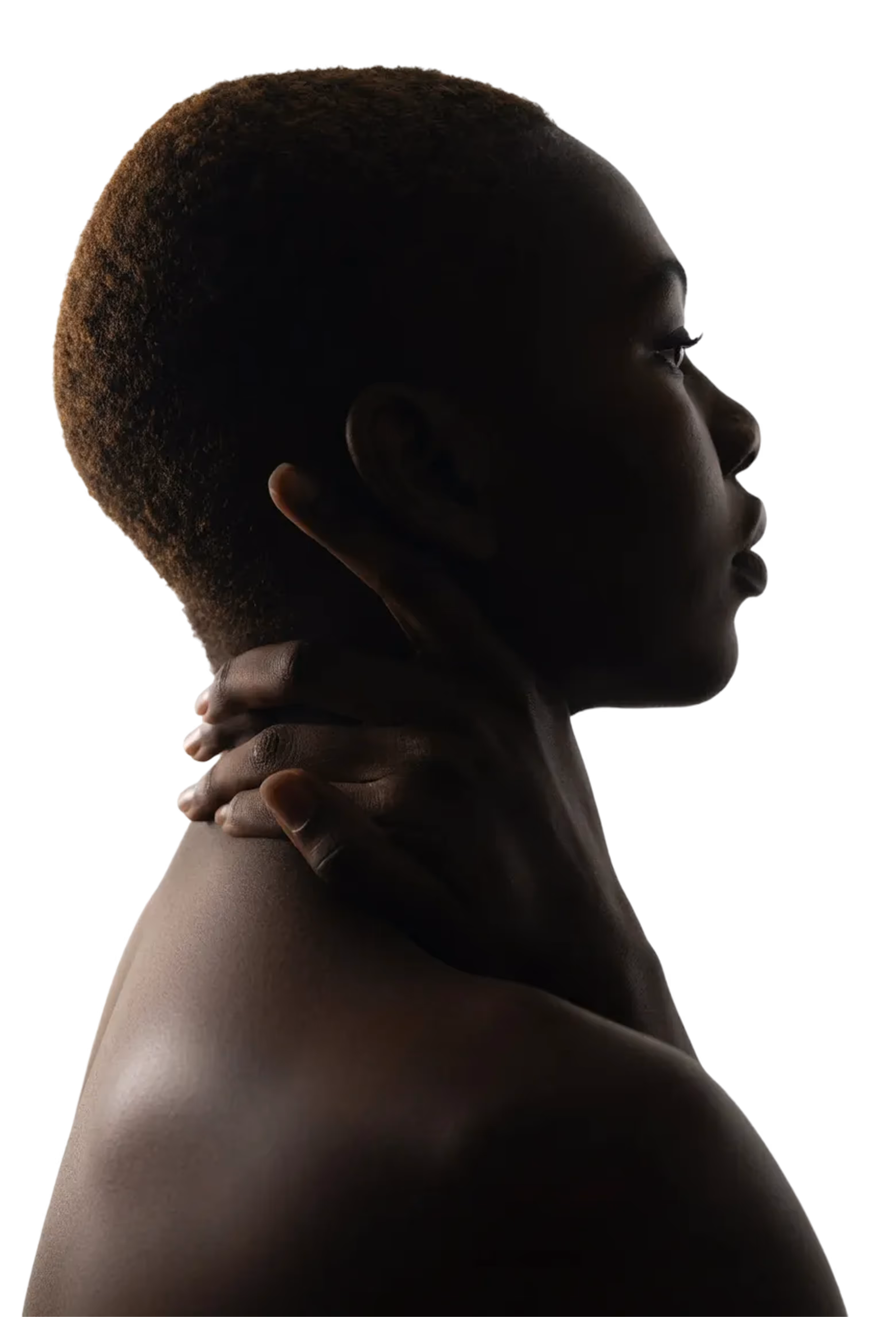Profile of a person with short curly hair touching the back of their neck against a black background.