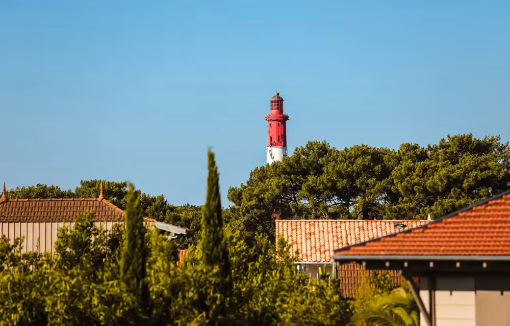 Glimpse of the Cap Ferret Lighthouse above rooftops and trees from the Village Junior Suite