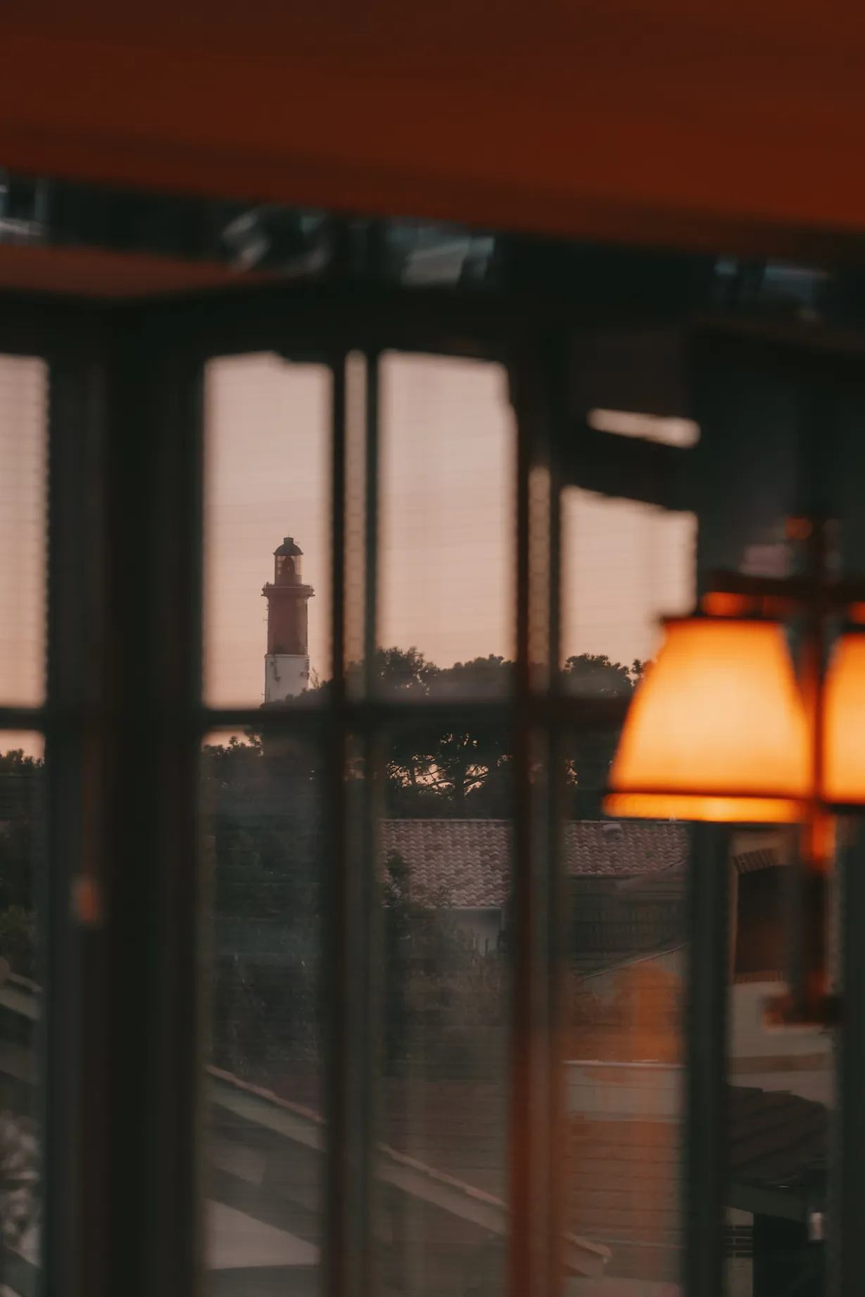 Vue depuis une chambre de la Villa Colette sur le phare de la Coubre au coucher du soleil, à travers une fenêtre à petits carreaux