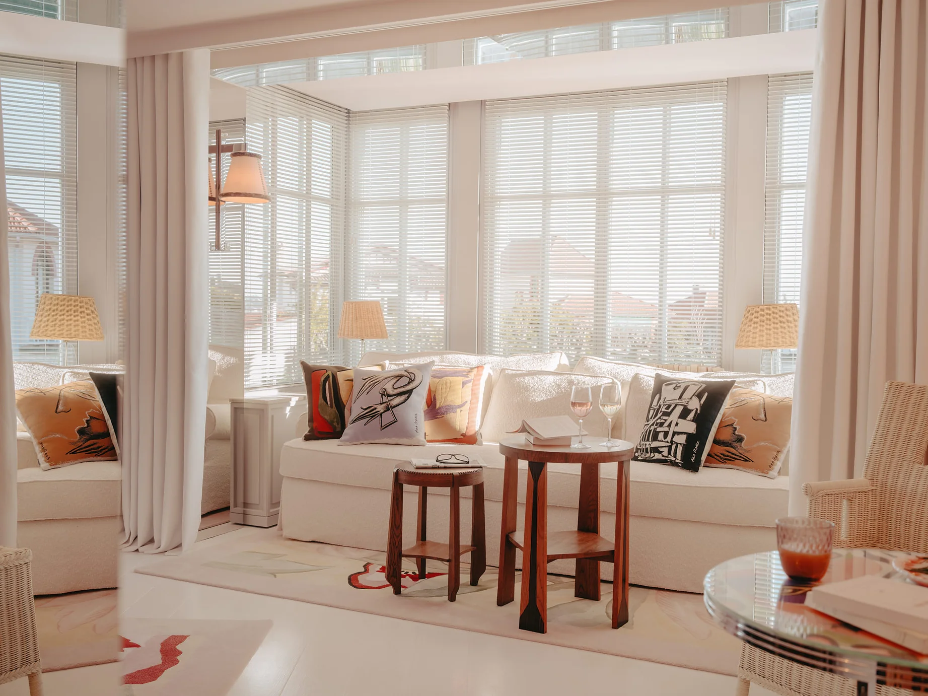 Salon lumineux de la Villa Colette avec banquette blanche, coussins artistiques, tabourets en bois et grande baie vitrée