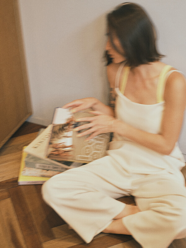 Blurry image of a woman sitting on the floor, holding and looking at stacked magazines.