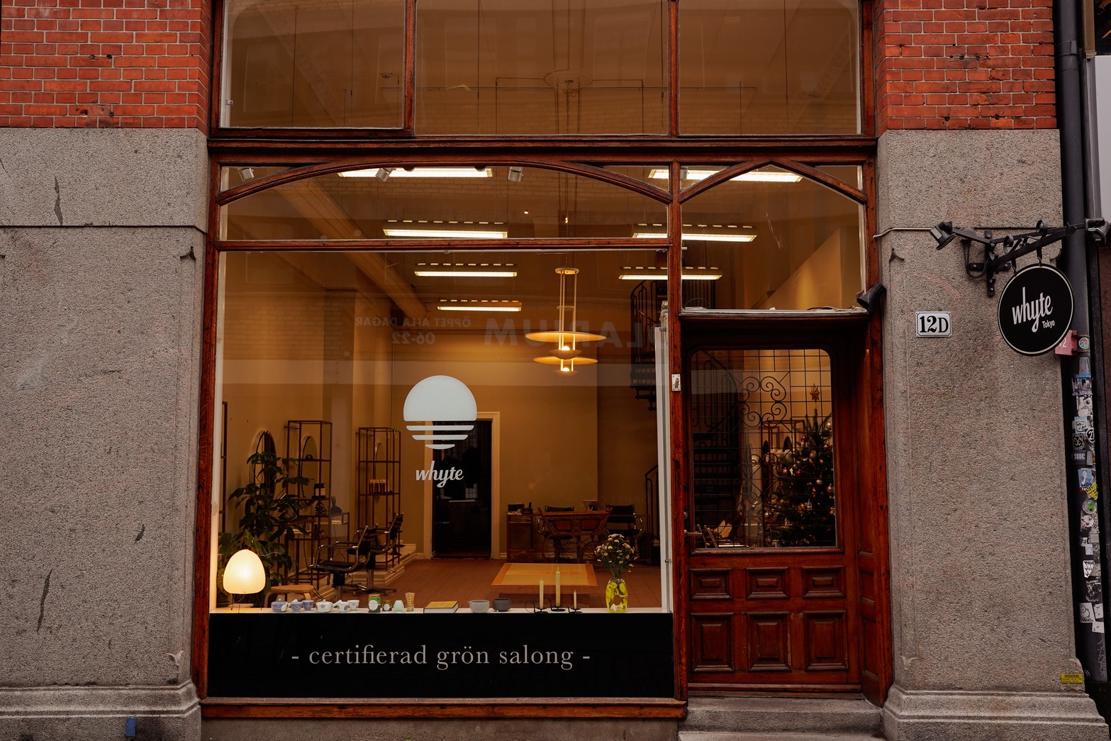 Front view of Whyte Tokyo, a salon with wooden framed glass windows and door, interior showing chairs, plants, and a Christmas tree.