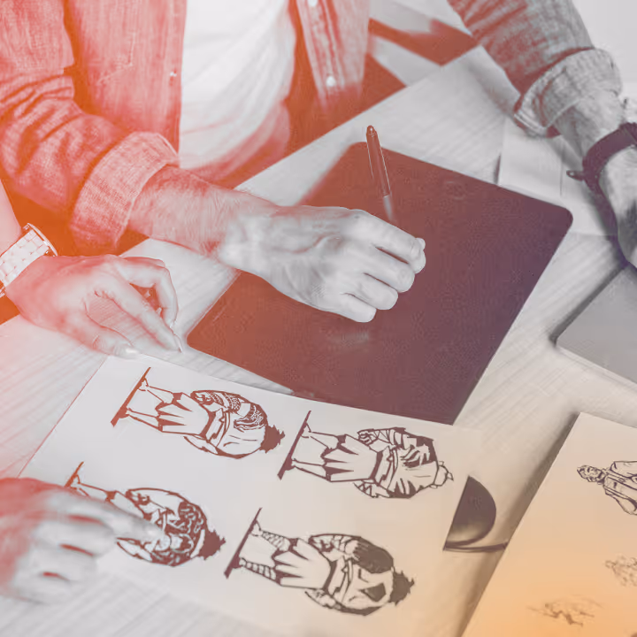 Two people reviewing cartoon character sketches while one holds a stylus over a drawing tablet.