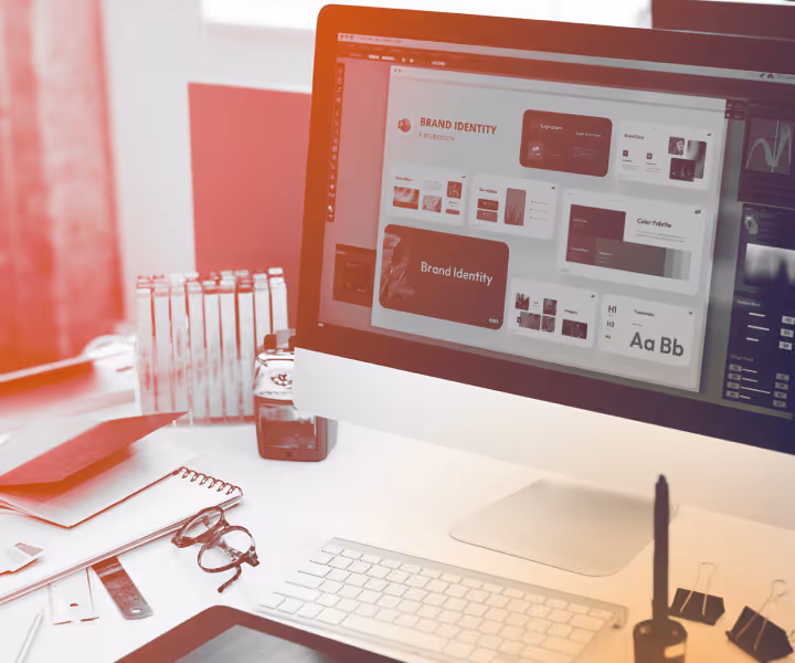 Desktop computer showing a brand identity design on screen with office supplies on the desk.