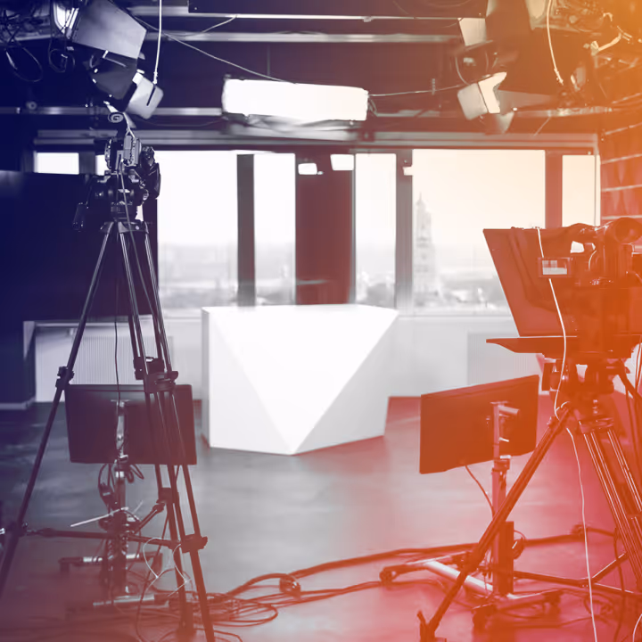 Film studio setup with cameras, lights, and a white geometric desk in front of large windows.