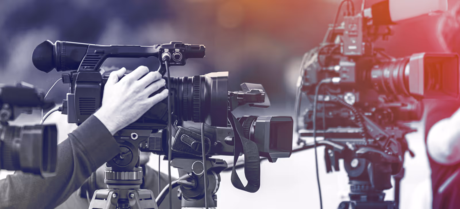 Close-up of professional video cameras on tripods with a hand adjusting one camera's controls.