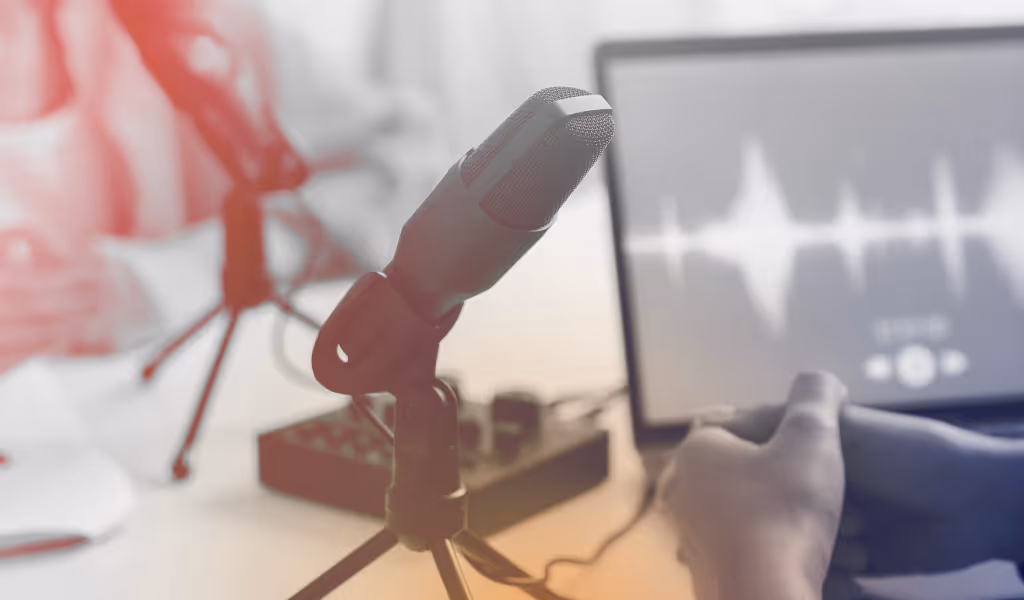 Close-up of a microphone on a tripod with audio editing software visible on a laptop screen.
