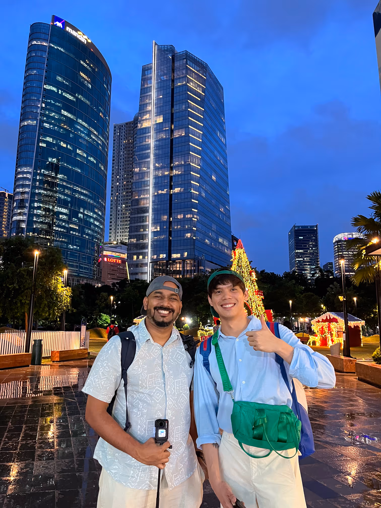 Two happy men posing at night with city skyscrapers and festive Christmas lights in the background.