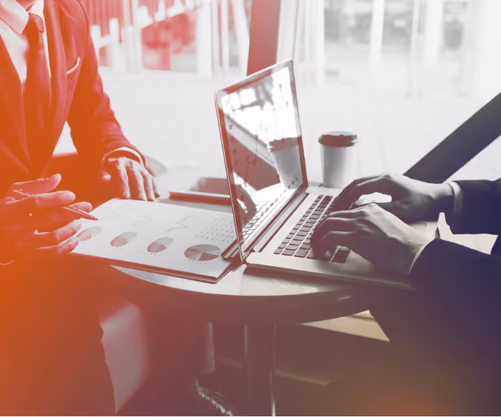 Two people at a round table with laptop and charts discussing business data.